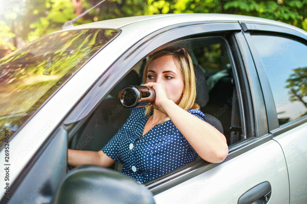 drunk girl driving a car. The girl drinks alcohol from a bottle while driving