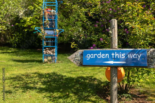 A blue sign post in garden directing the way, lots of green and blue, nobody in the image