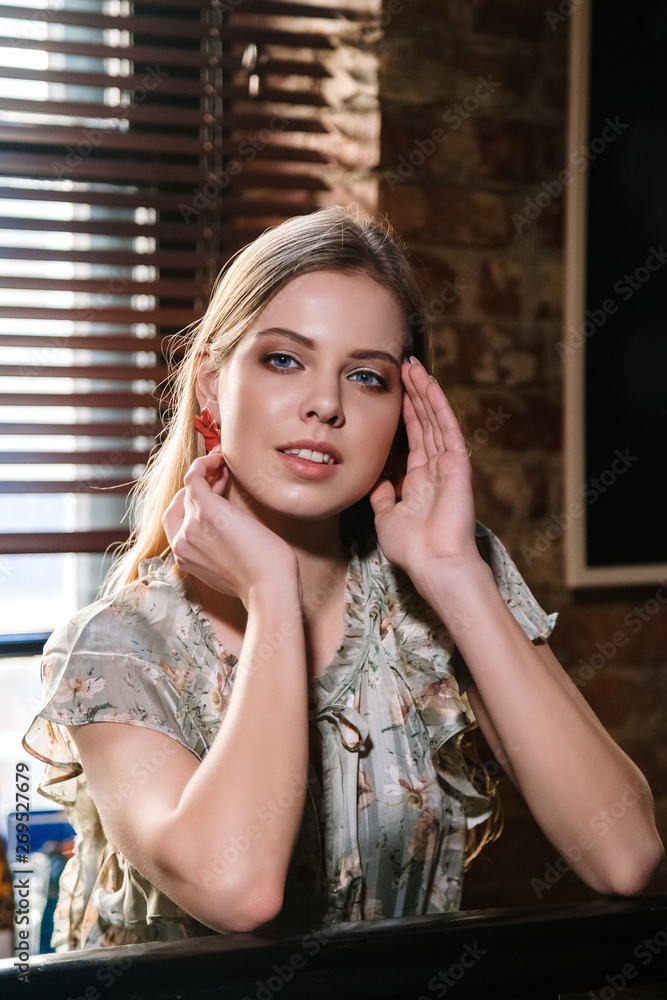 Fototapeta premium beautiful girl with natural blond hair and blue eyes is sitting at the bar counter and smiling