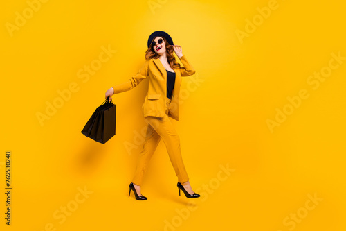 Full length side profile body size photo beautiful she her lady walking down street carry new clothes packs perfect look traveler wear specs formal-wear costume suit isolated yellow bright background