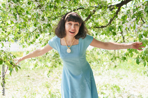 Beautiful woman in a long blue dress with flowering apple trees in the spring garden
