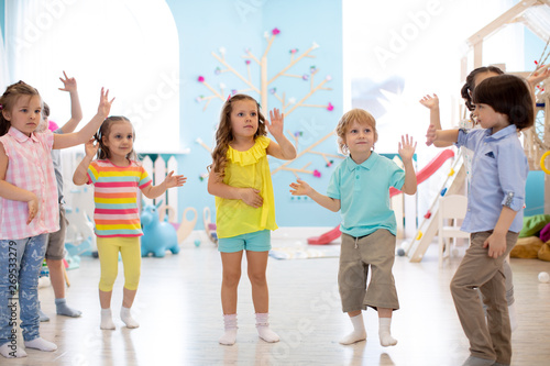 Happy children having fun dancing indoors in a sunny room at day care or entertainment center