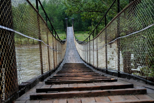 Fototapeta Naklejka Na Ścianę i Meble -  A beautiful,long wooden swinging bridge over a mountain river with wire railings