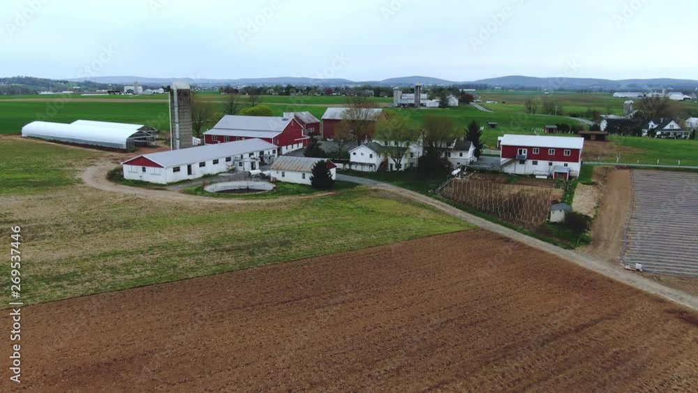 Colorful ranch with white and red painted buildings, surrounded with plowed fields and green meadows, spring in Pennsylvania, travel, agriculture, and landscape Colorful ranch with white and red painted buildings, surrounded with plowed fields and green meadows, spring in Pennsylvania, travel, agriculture, and landscape