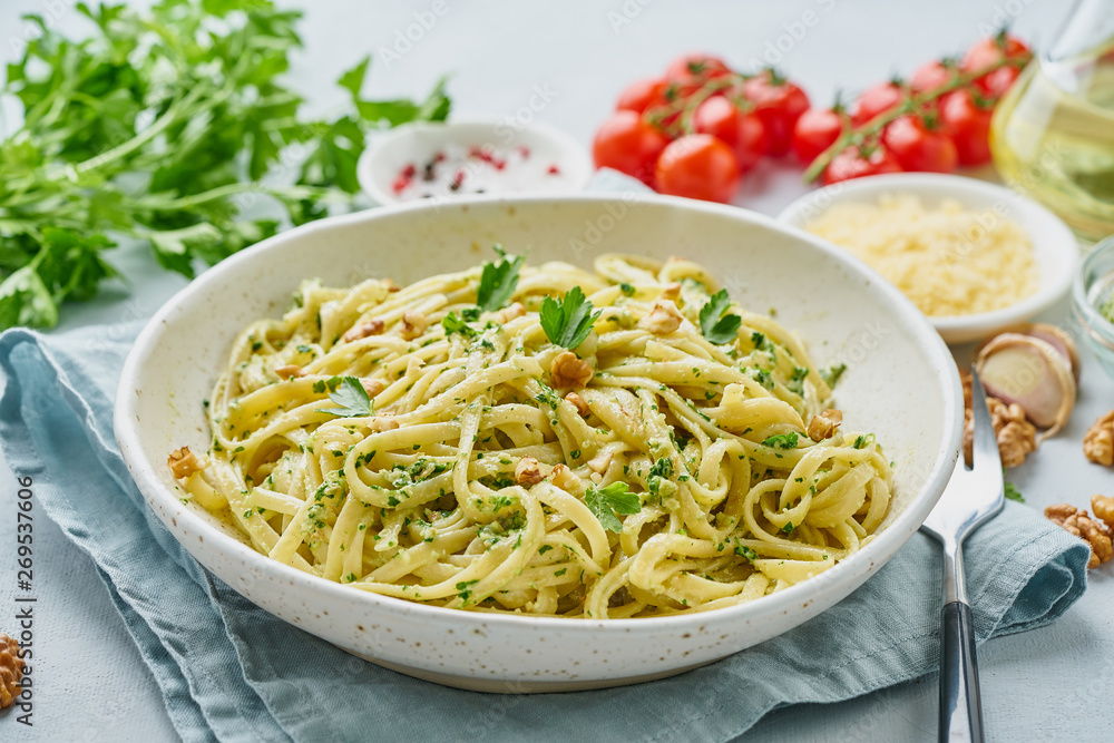 Pesto pasta, bavette with walnuts, parsley, garlic, nuts, olive oil. Side view, close-up, blue background.