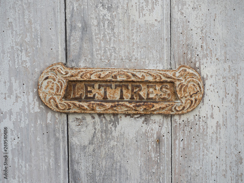 close up of letter box in France says lettres set in a wooden door.The box is vintage and shows rust photo