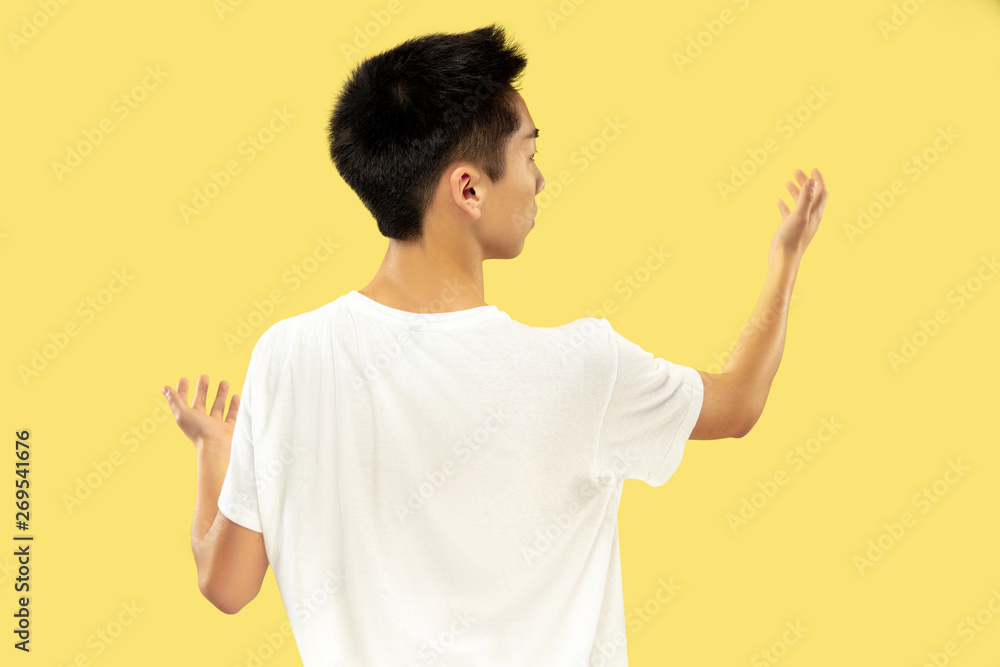Korean young man's half-length portrait on yellow studio background. Male model in white shirt. Pointing up to the place for your ad. Concept of human emotions, facial expression. Trendy colors. Korean young man's half-length portrait on yellow studio background. Male model in white shirt. Pointing up to the place for your ad. Concept of human emotions, facial expression. Trendy colors.