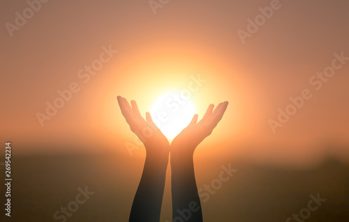 Free concept: Raised hands catching sun on sunset sky