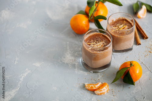 Glass of hot tangerine orange cocoa or chocolate decorated citrus peel on gray background with copy space top view.Horizontal orientation photo