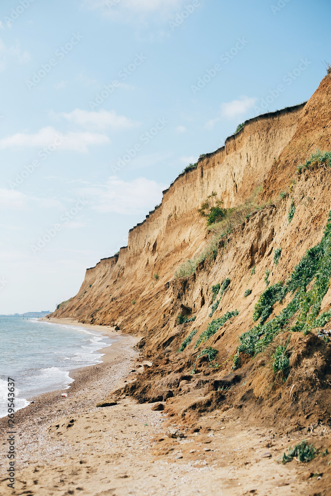 Beautiful sandy cliff with grass and sea waves on beach with on tropical island. Big rock and waves in ocean bay or lagoon. Tranquil calm moment. Summer vacation. Copy space
