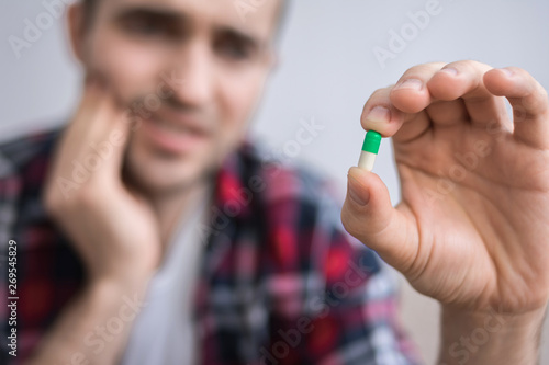 Male suffering from strong tooth pain, man with pill, holding a pill, sitting on the couch, close up
