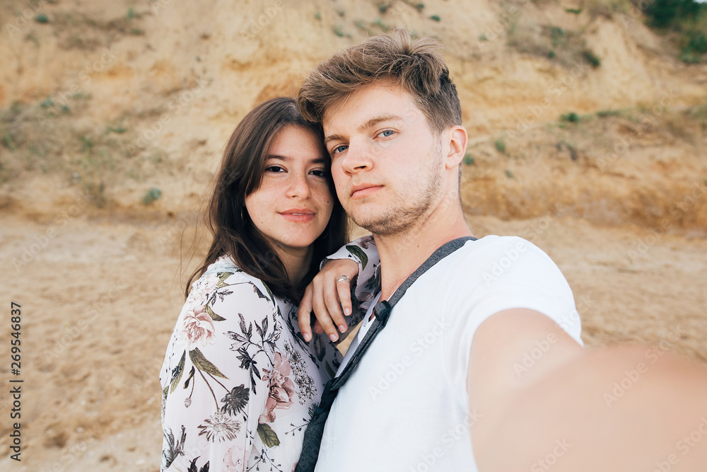 Stylish hipster couple taking selfie on beach at sandy cliff at sea. Summer vacation. Portrait of happy young family on honeymoon on tropical island making selfie. Space for text Stylish hipster couple taking selfie on beach at sandy cliff at sea. Summer vacation. Portrait of happy young family on honeymoon on tropical island making selfie. Space for text
