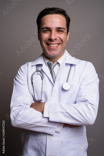 Handsome Persian man doctor against gray background