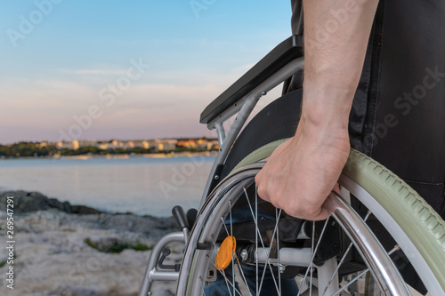 Disabled man sitting on wheelchair near sea at sunset. photo