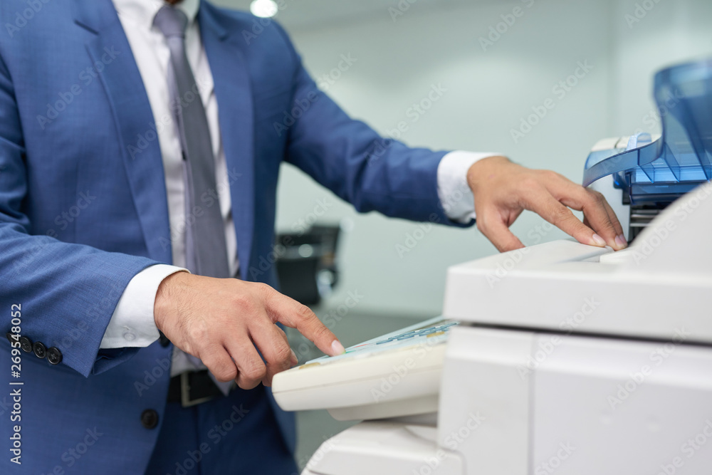Close-up of businessman in suit standing near the copy machine and making a copy of document at office Close-up of businessman in suit standing near the copy machine and making a copy of document at office