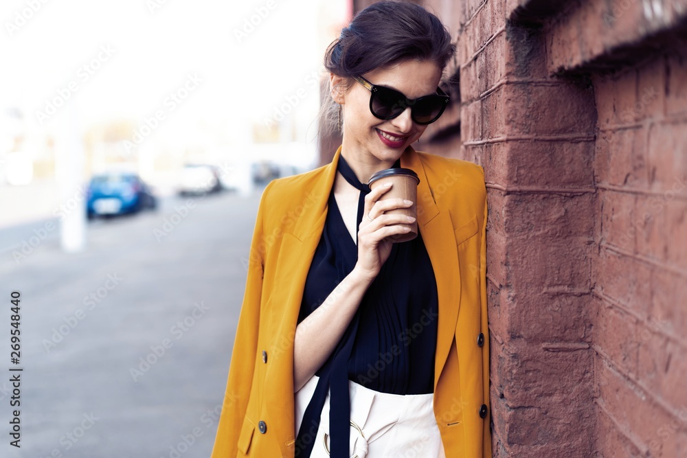 Fototapeta premium Portrait fashion woman in sunglasses walking on street . She wears yellow jacket, smiling to side.