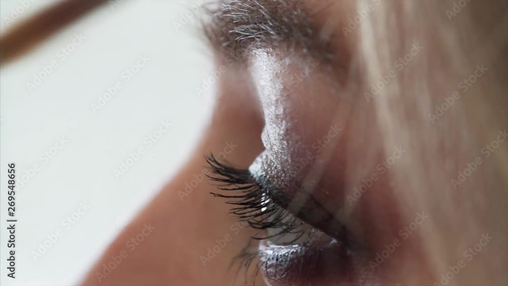 Extreme close view of female eye. Makeup artist is making makeup for woman, painting eyebrows before photo shoot Extreme close view of female eye. Makeup artist is making makeup for woman, painting eyebrows before photo shoot