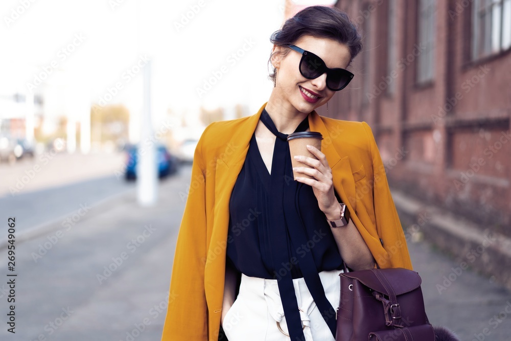 Obraz premium Portrait fashion woman in sunglasses walking on street . She wears yellow jacket, smiling to side.