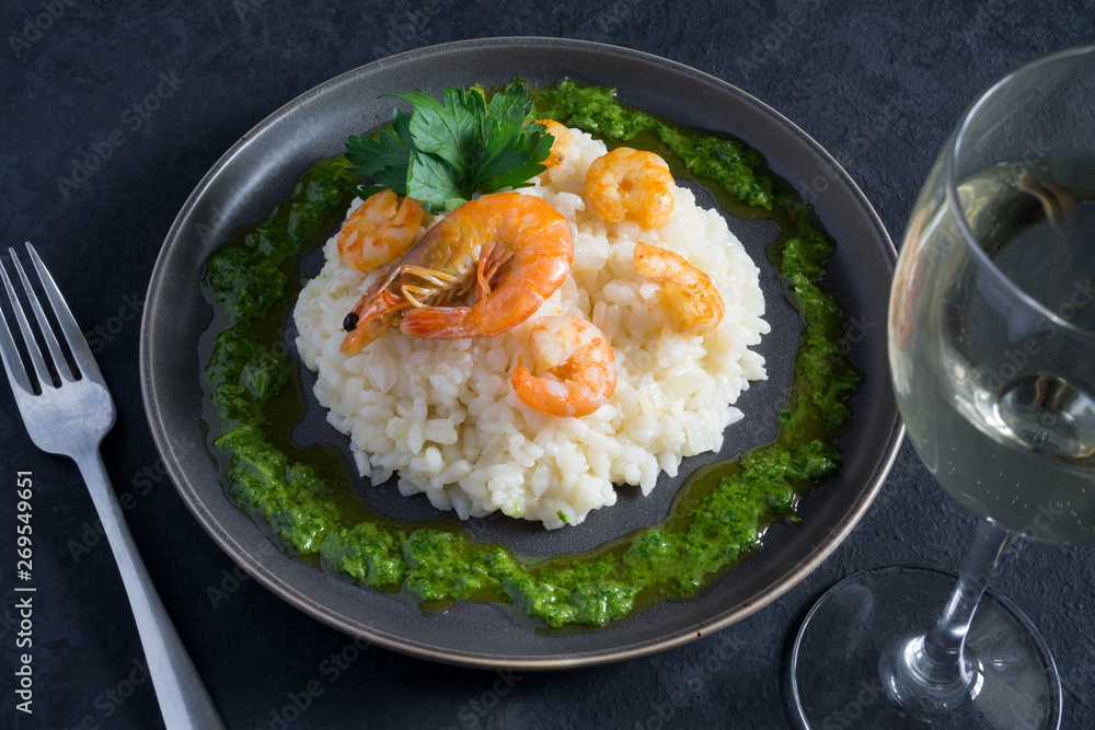Risotto with shrimps, parsley, green sauce and a glass of white wine on a gray plate on a dark gray background with copy space. Italian food Risotto with shrimps, parsley, green sauce and a glass of white wine on a gray plate on a dark gray background with copy space. Italian food