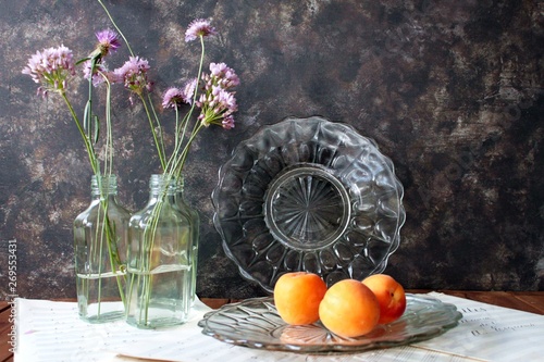 Flores lila en botellas de Crista y albaricoques en plato de cristal photo