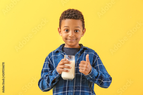 Cute African-American boy with glass of milk showing thumb-up on color background