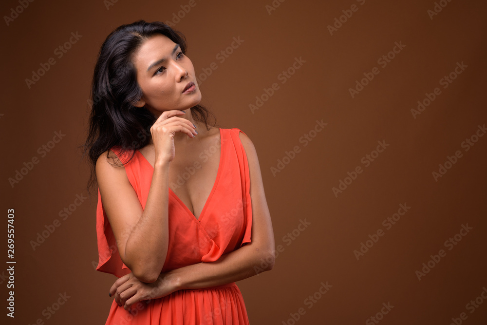 Studio shot of beautiful Asian woman against brown background Studio shot of beautiful Asian woman against brown background