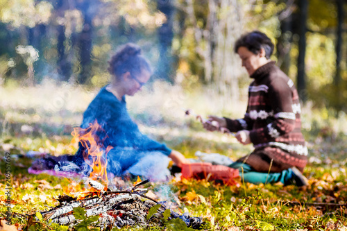 A girl and a woman are preparing a barbecue in the autumn forest near the fire_