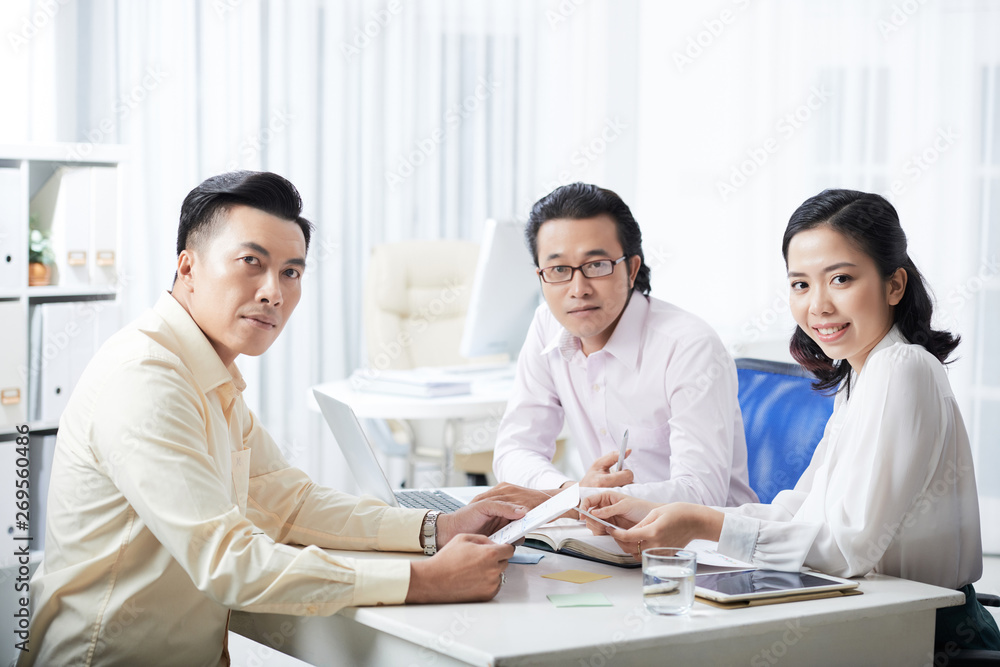 Portrait of young Asian business people working at the table in team and looking at camera during meeting at office Portrait of young Asian business people working at the table in team and looking at camera during meeting at office