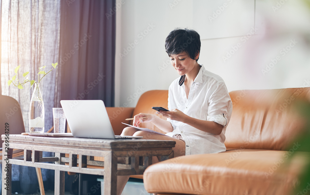 Asian self employed woman sitting on couch & working on laptop at home Asian self employed woman sitting on couch & working on laptop at home