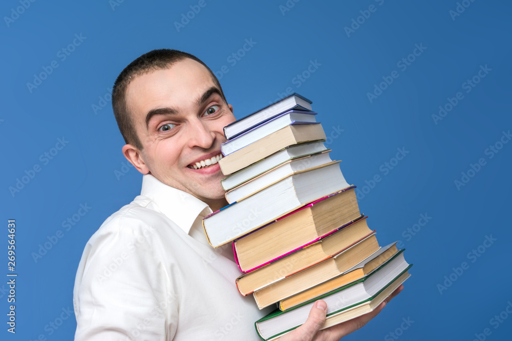 Portrait, attractive man in the white shirt with books, smiling, looking at the camera, close up, the concept of heavy loads in education, blue background, front view Portrait, attractive man in the white shirt with books, smiling, looking at the camera, close up, the concept of heavy loads in education, blue background, front view