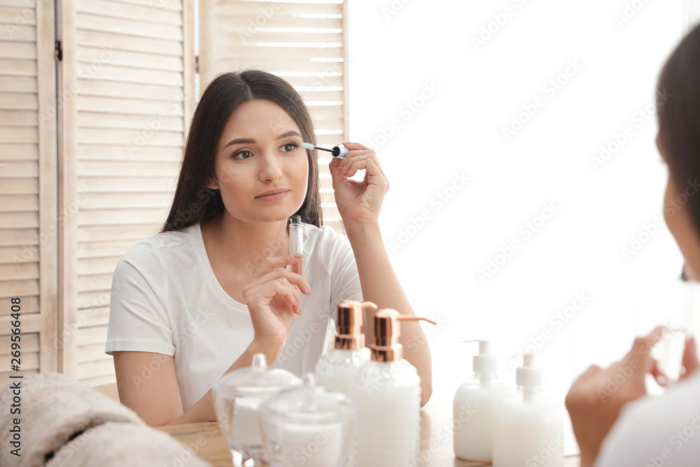 Beautiful woman applying oil onto her eyelashes near mirror indoors Beautiful woman applying oil onto her eyelashes near mirror indoors
