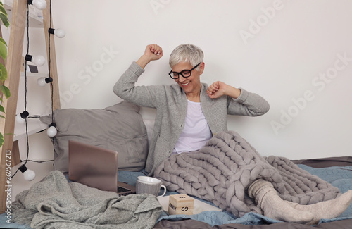 Woman covered with soft woolen blanket, relaxing at home,drinking cacao, using laptop. Cozy and comfy lifestyle