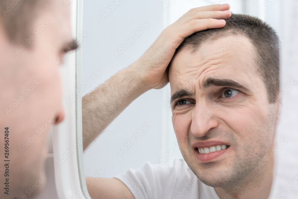 Obraz premium Tired man, guy looks in the mirror, close up