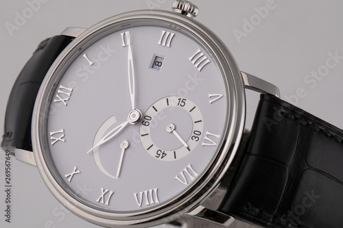 Silver wristwatch with white dial, silver clockwise, stopwatch and chronograph on black leather strap isolated on white background.