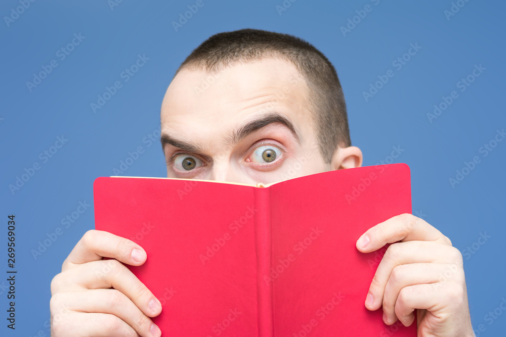 Male reads the book, stares in surprise at the camera, raise his eyebrows, facial expressions, close up, copy space, for advertising Male reads the book, stares in surprise at the camera, raise his eyebrows, facial expressions, close up, copy space, for advertising
