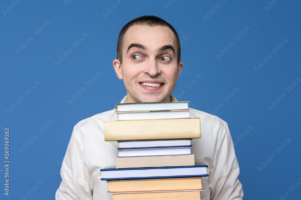 Male in the white shirt with books, looking to the side, concept of heavy loads in education, copy space, advertising, slogan, blue background Male in the white shirt with books, looking to the side, concept of heavy loads in education, copy space, advertising, slogan, blue background