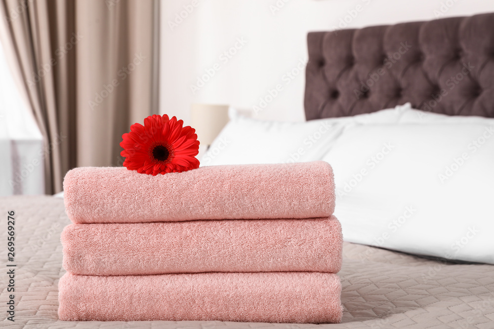 Stack of fresh towels with flower on blanket in bedroom. Space for text Stack of fresh towels with flower on blanket in bedroom. Space for text