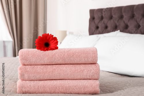 Stack of fresh towels with flower on blanket in bedroom. Space for text
