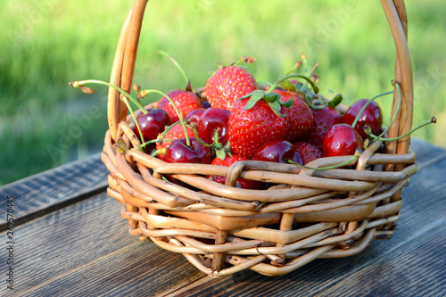 Strawberries and cherries in a basket on a natural background. Fresh organic summer berries