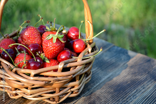 Strawberries and cherries in a basket on a natural background. Fresh organic summer berries