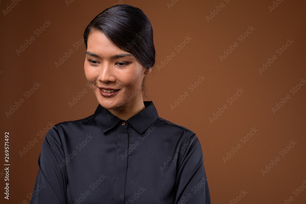 Studio shot of beautiful Asian businesswoman against brown backg Studio shot of beautiful Asian businesswoman against brown backg