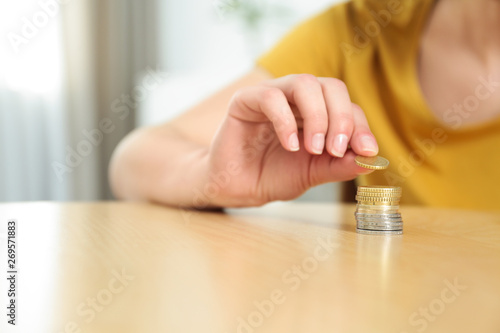 Woman stacking coins on table at home, closeup. Space for text