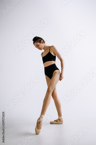 Fototapeta Naklejka Na Ścianę i Meble -  Fashion ballet. Young female ballet dancer in black bodysuit against white studio background. Caucasian ballerina like a fashion model. Style, contemporary choreography concept. Creative art photo.