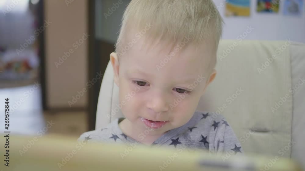 Cute little boy, eating porridge for breakfast at home, while watching cartoon on tablet. Children and technology or healthy food for kid concept. Cute little boy, eating porridge for breakfast at home, while watching cartoon on tablet. Children and technology or healthy food for kid concept.