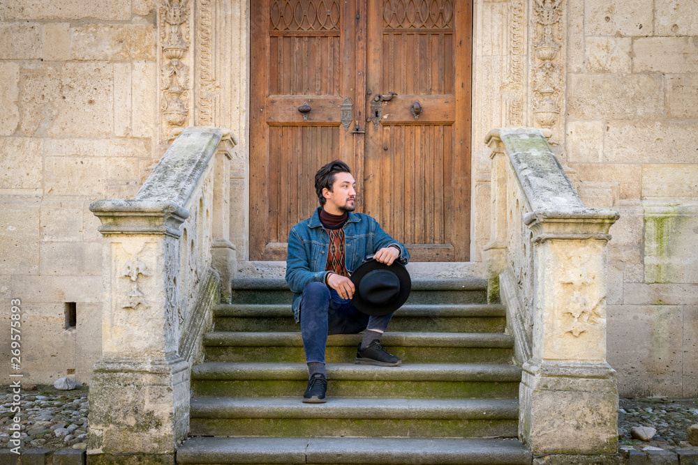 Portrait of a young man sitting against a beautiful old medieval cathedral door. A man in front of a an old architecture church entrance door in Alba Iulia, Romania