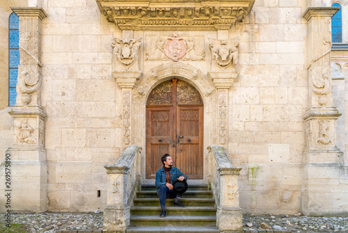 Obraz na płótnie Portrait of a young man sitting against a beautiful old medieval cathedral door. A man in front of a an old architecture church entrance door in Alba Iulia, Romania w salonie