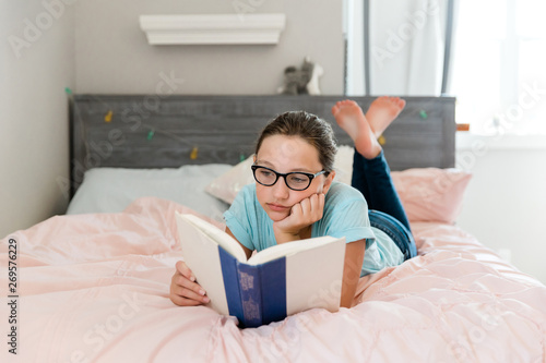 Tween Teen Girl With Glasses Quietly Reading a Book in her bedroom on the bed