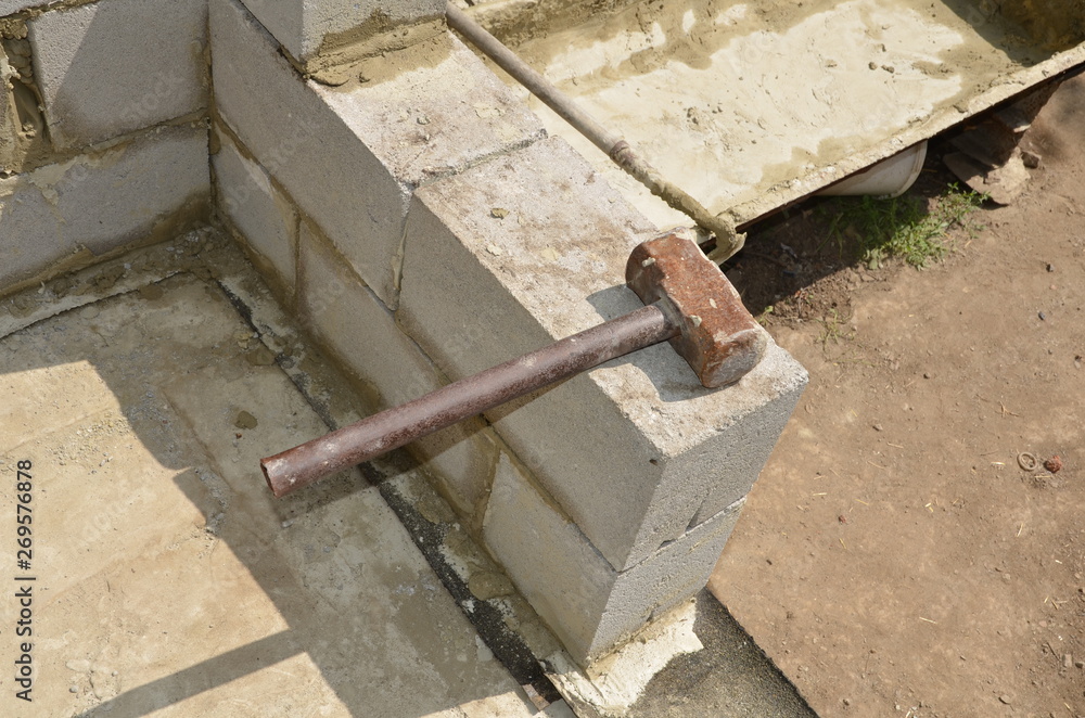 The iron hammer lies on the cinder block on the background of the pan for mixing mortar. The iron hammer lies on the cinder block on the background of the pan for mixing mortar.