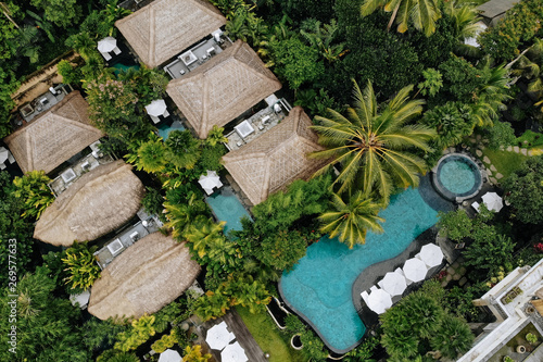 Aerial view of luxury hotel with straw roof villas and pools in tropical jungle and palm trees. Luxurious villa, pavilion in forest, Ubud, Bali