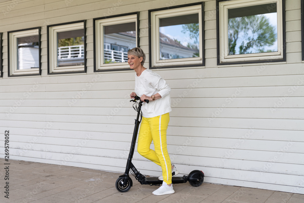 Sportliche Frau mit Elektroroller vor Hauswand Sportliche Frau mit Elektroroller vor Hauswand